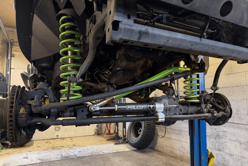 Automotive service in Mertztown, PA, at E-Motive Performance & Auto Repair. Close-up of a lifted Jeep's upgraded front suspension system featuring heavy-duty coil springs, steering stabilizer, control arms, and steering components, highlighting professional suspension upgrades, off-road performance enhancements, and precision steering modifications for improved handling and durability.